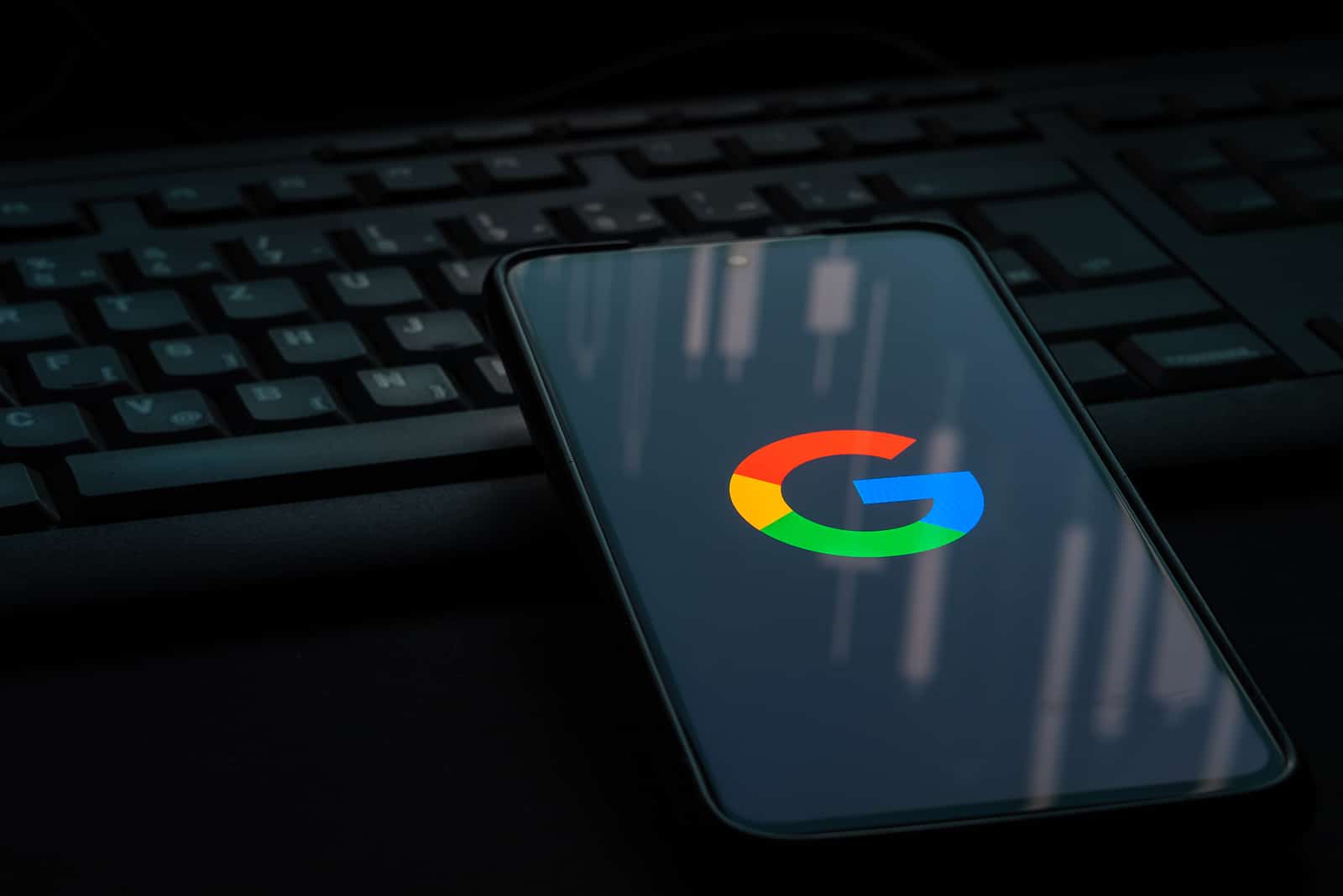 A dark phone and keyboard with the Google logo on smartphone screen